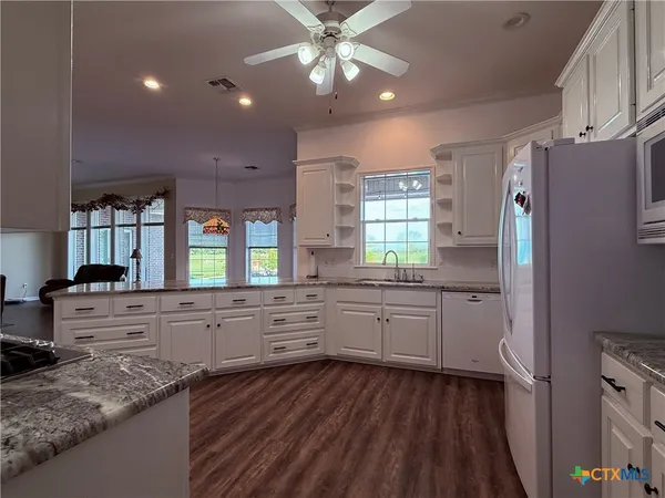 a kitchen with stainless steel appliances granite countertop a refrigerator a sink dishwasher a stove and white countertops with wooden floor