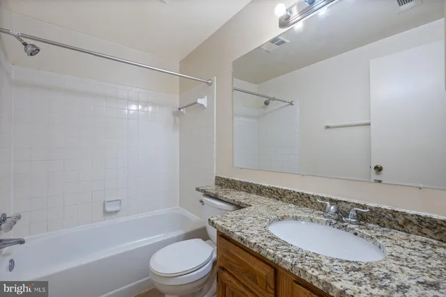 a bathroom with a granite countertop sink a toilet a mirror a bathtub and shower