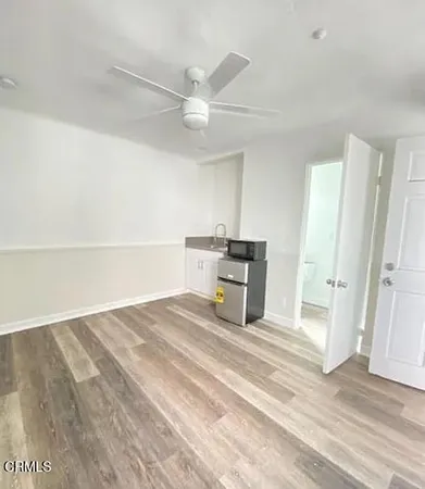 a view of an empty room with wooden floor and a ceiling fan