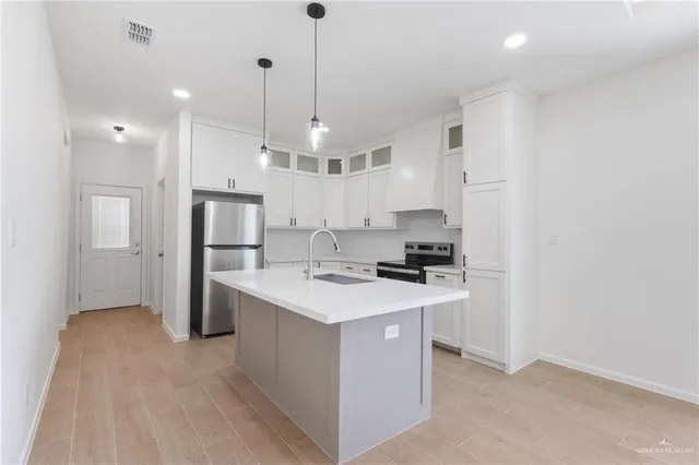 a kitchen with stainless steel appliances a refrigerator a sink dishwasher a stove and white cabinets with wooden floor