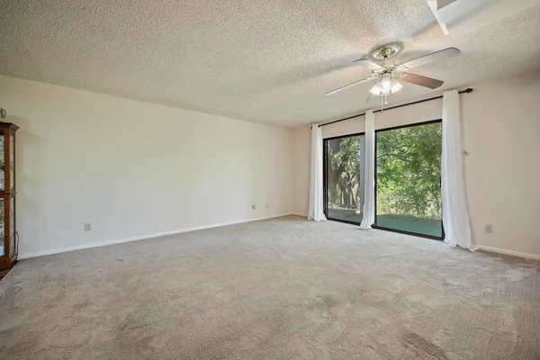 an empty room with chandelier fan and windows