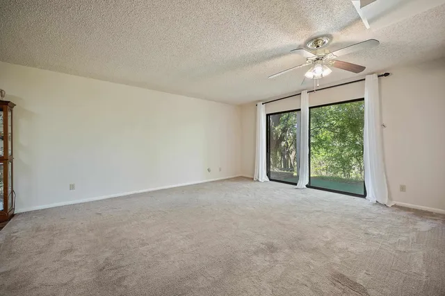 an empty room with chandelier fan and windows