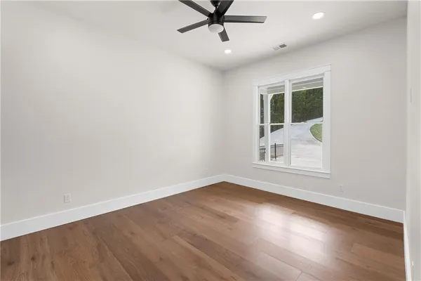 an empty room with wooden floor chandelier fan and windows