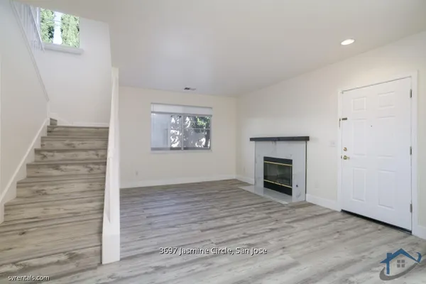 a view of an empty room with wooden floor fireplace and a window