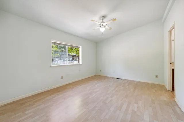 an empty room with wooden floor chandelier fan and windows