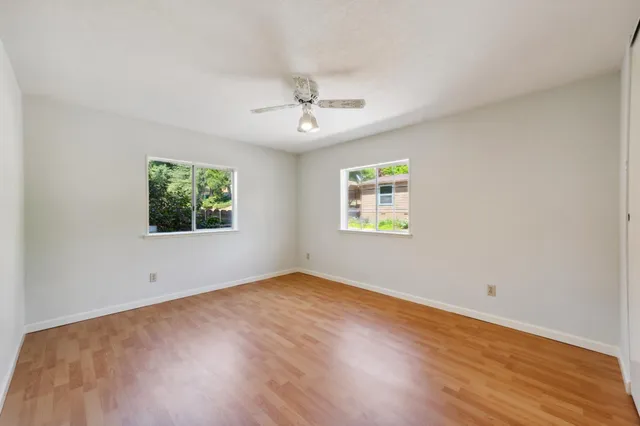 an empty room with wooden floor ceiling fan and windows