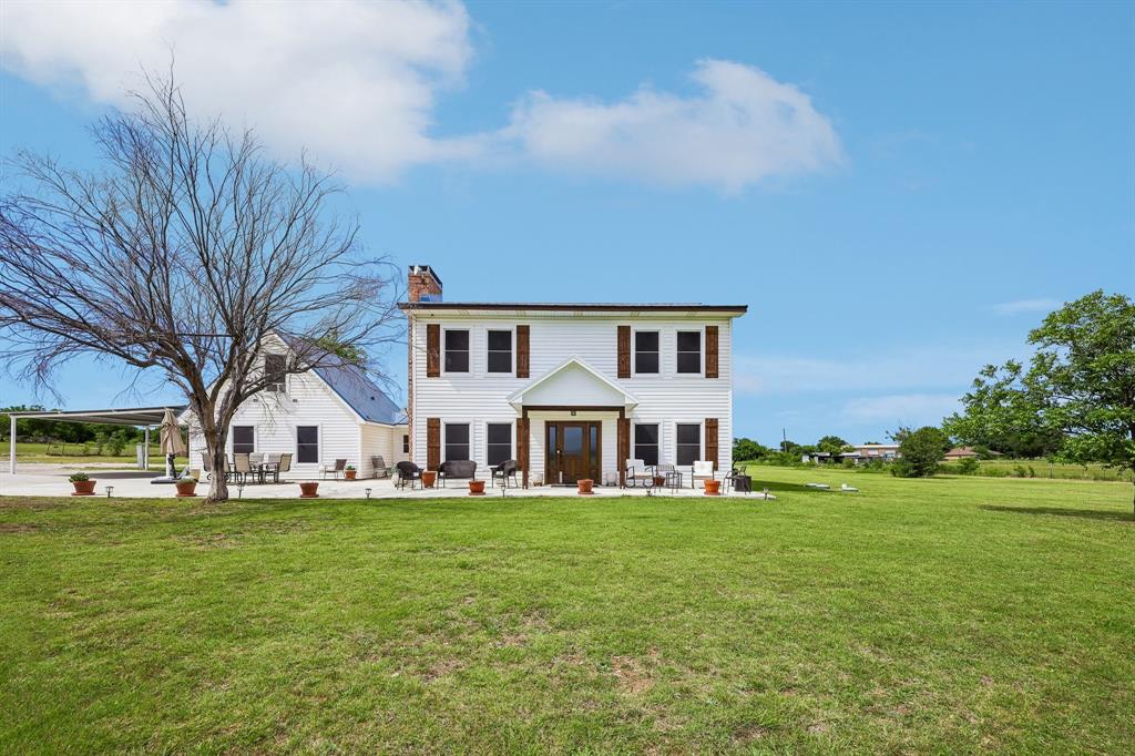 Two-story white exterior with dark shutters, front porch, and expansive green lawn