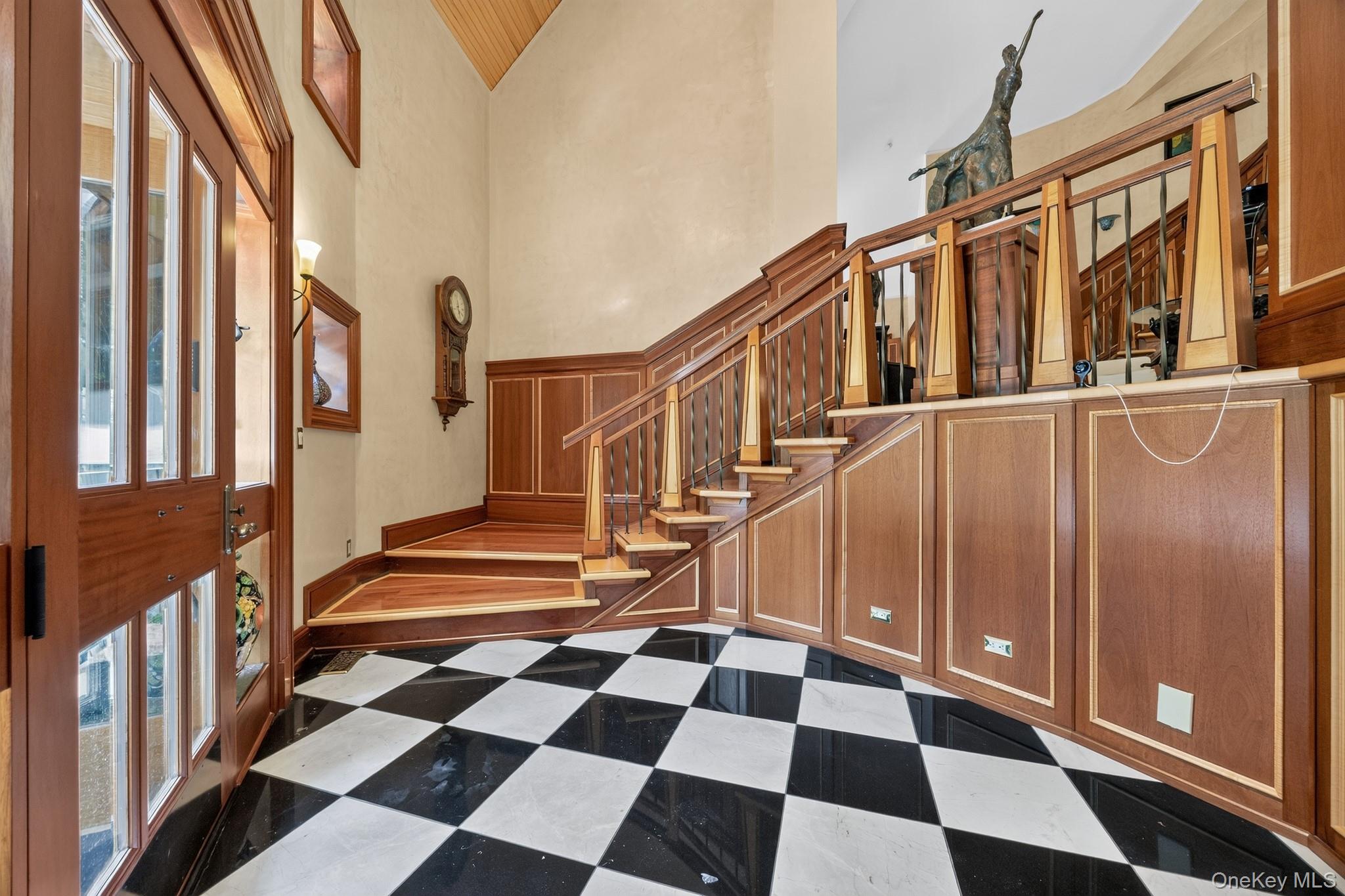 23 Inningwood Road Ossining, NY 10562 - Photo 9 of 50 Foyer featuring black and white checkerboard flooring, a multi-paneled wood entry door, a sweeping wood staircase with decorative balusters, extensive wood paneling, and a vaulted wood-paneled ceiling