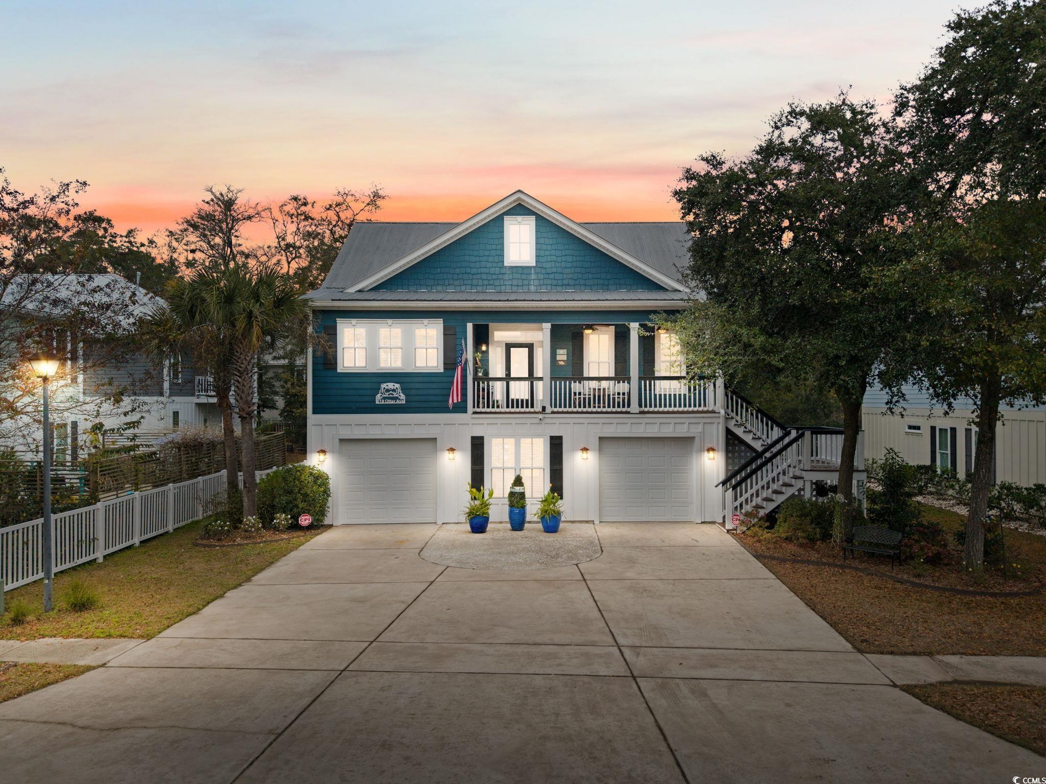 Beach home with concrete driveway, stairway, an attached garage, and covered porch