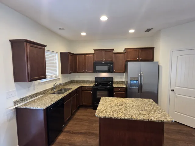 a kitchen with kitchen island granite countertop stainless steel appliances a sink stove refrigerator and wooden cabinets