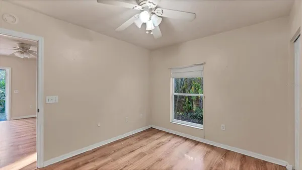 an empty room with wooden floor chandelier fan and windows