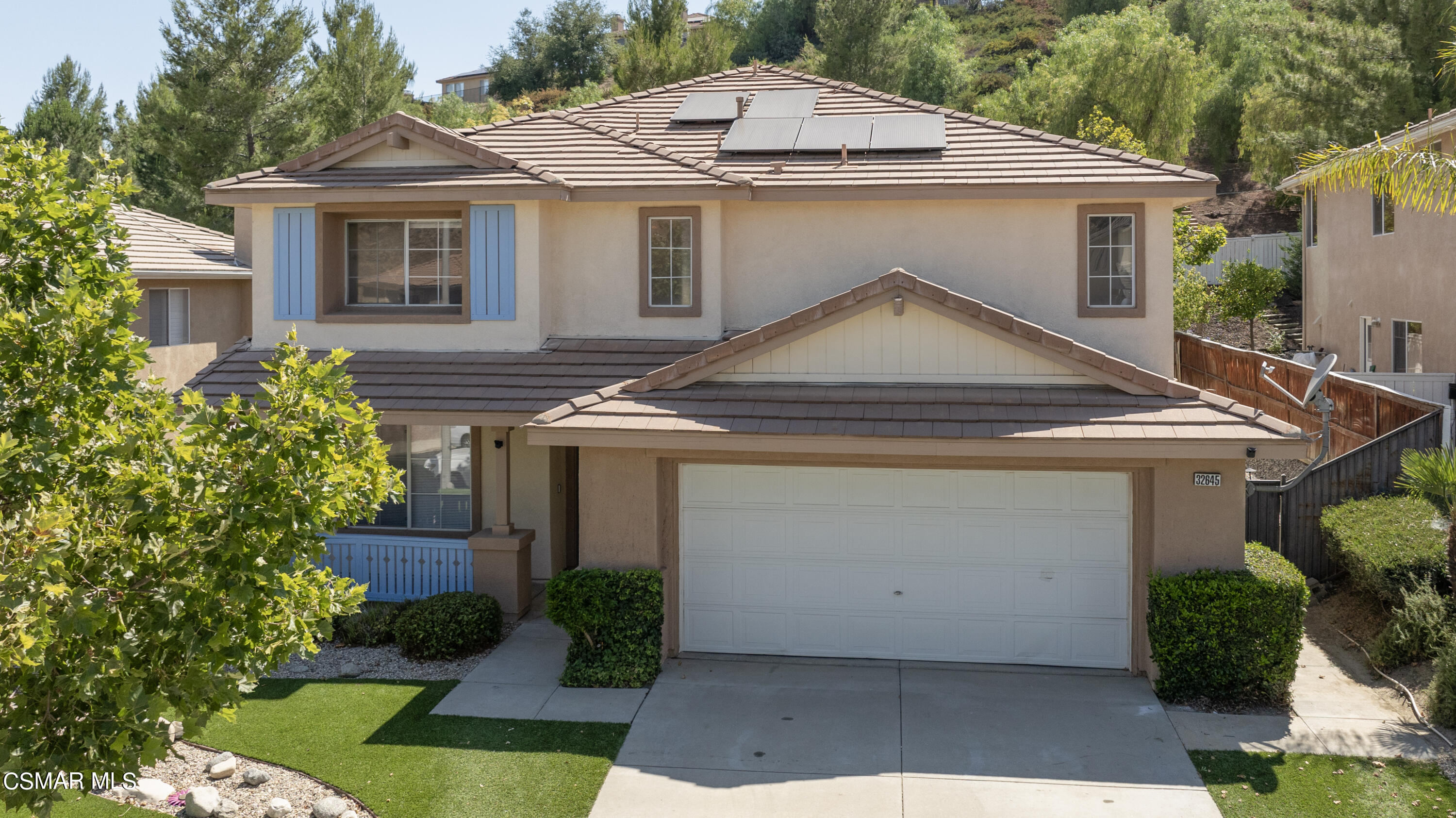 a white house with a small yard plants and a large tree