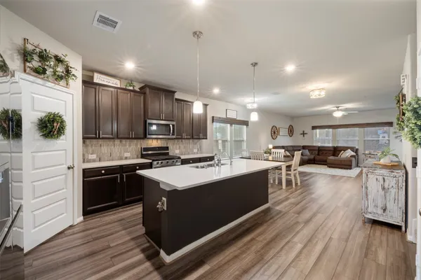 a kitchen with stainless steel appliances kitchen island granite countertop a stove top oven a sink dishwasher a refrigerator and cabinets with wooden floor
