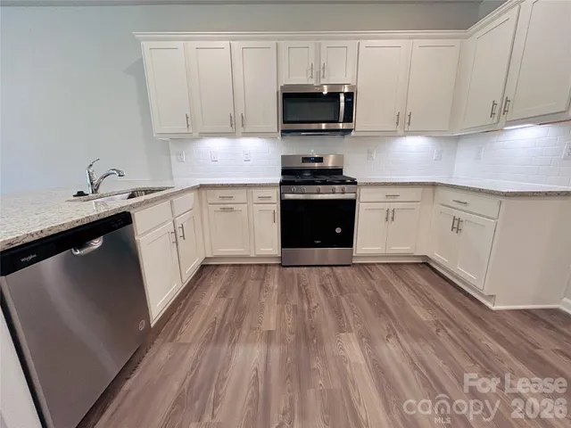a kitchen with granite countertop a sink dishwasher a stove and a microwave oven with cabinets
