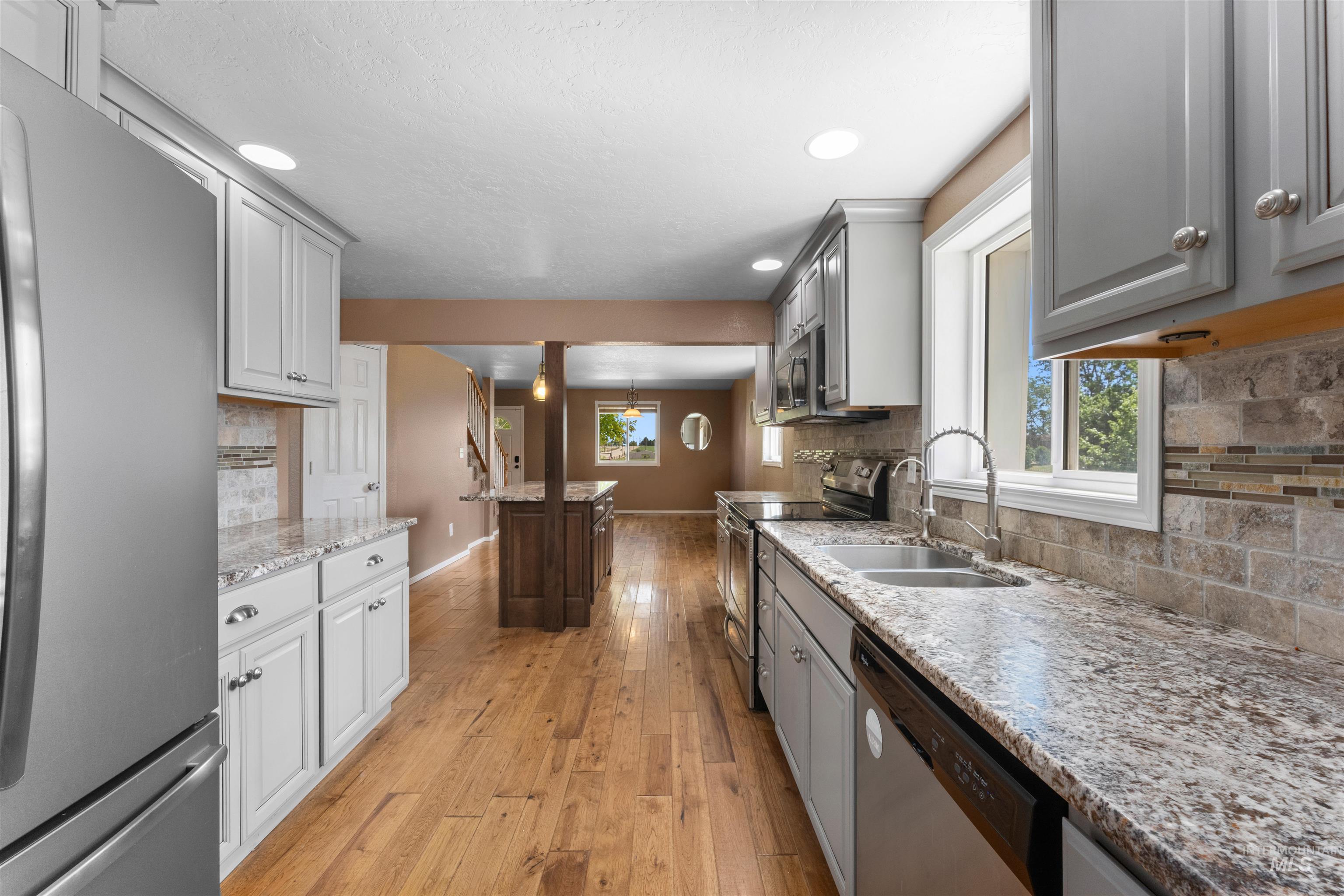 17441 Upper Pleasant Ridge Road Caldwell, ID 83607 - Photo 14 of 40 Kitchen featuring light wood-finish flooring, two-tone cabinetry, stone countertops, and a tiled backsplash