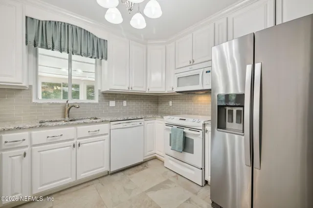 a kitchen with stainless steel appliances granite countertop a refrigerator a sink and white cabinets