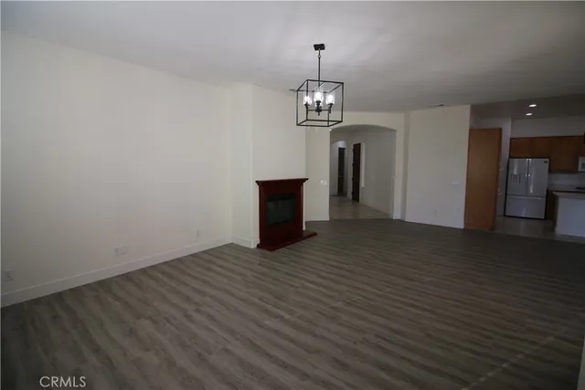 an empty room with wooden floor fireplace and kitchen view