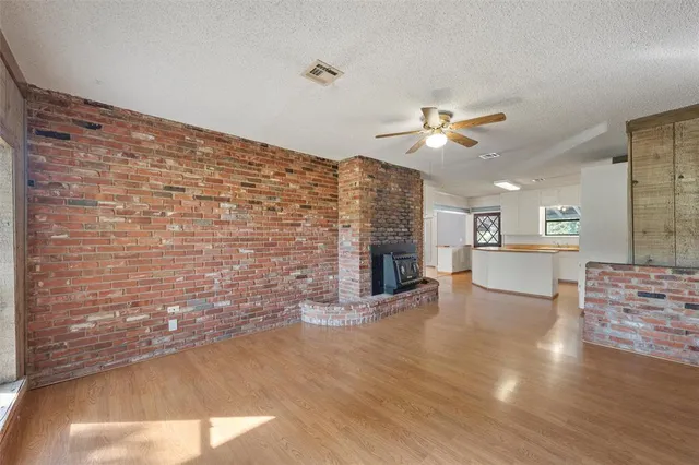 a view of an empty room and kitchen with fireplace ceiling fan and wooden floor