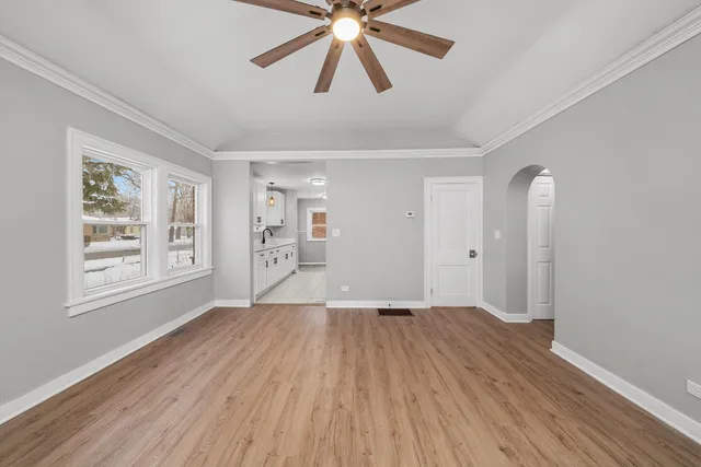 an empty room with wooden floor chandelier fan and windows