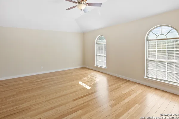 an empty room with wooden floor fan and windows