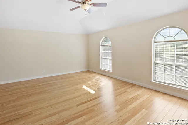 an empty room with wooden floor fan and windows