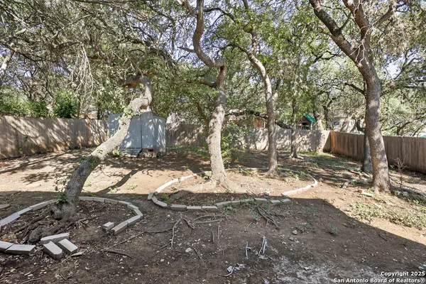 a backyard of a house with large trees and wooden fence