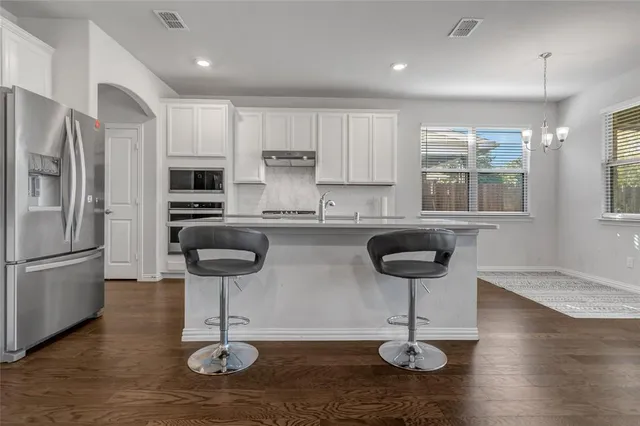 a kitchen with stainless steel appliances granite countertop a refrigerator a stove a sink cabinets and a dining table with wooden floor