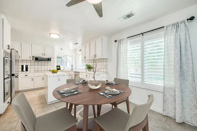 a kitchen with stainless steel appliances kitchen island granite countertop a dining table chairs and a refrigerator