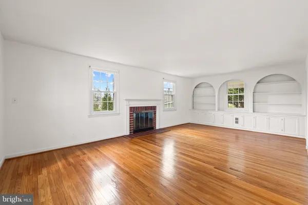 an empty room with wooden floor fireplace and windows