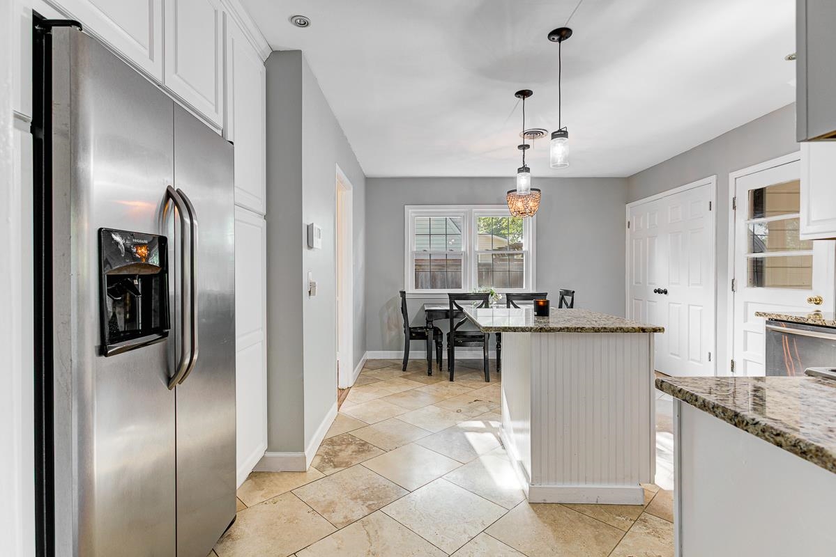 5676 Barfield Road Memphis, TN 38120 - Photo 7 of 19 Stainless steel side-by-side refrigerator, white upper cabinetry, light-toned tiled flooring, a kitchen island with beadboard paneling and a granite countertop, and pendant lighting fixtures