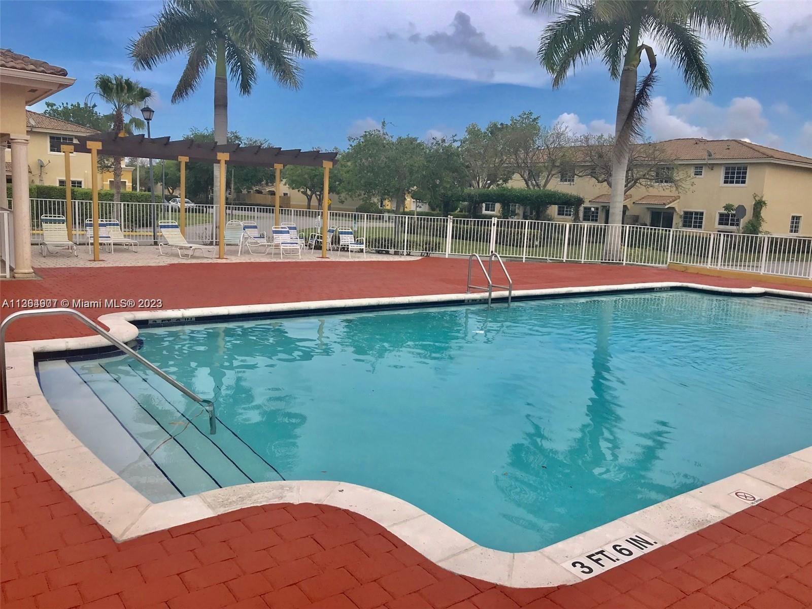 13974 Southwest 260th Street, Unit 102 Homestead, FL 33032 - Photo 14 of 16 a view of a swimming pool with a lawn chairs under an umbrella