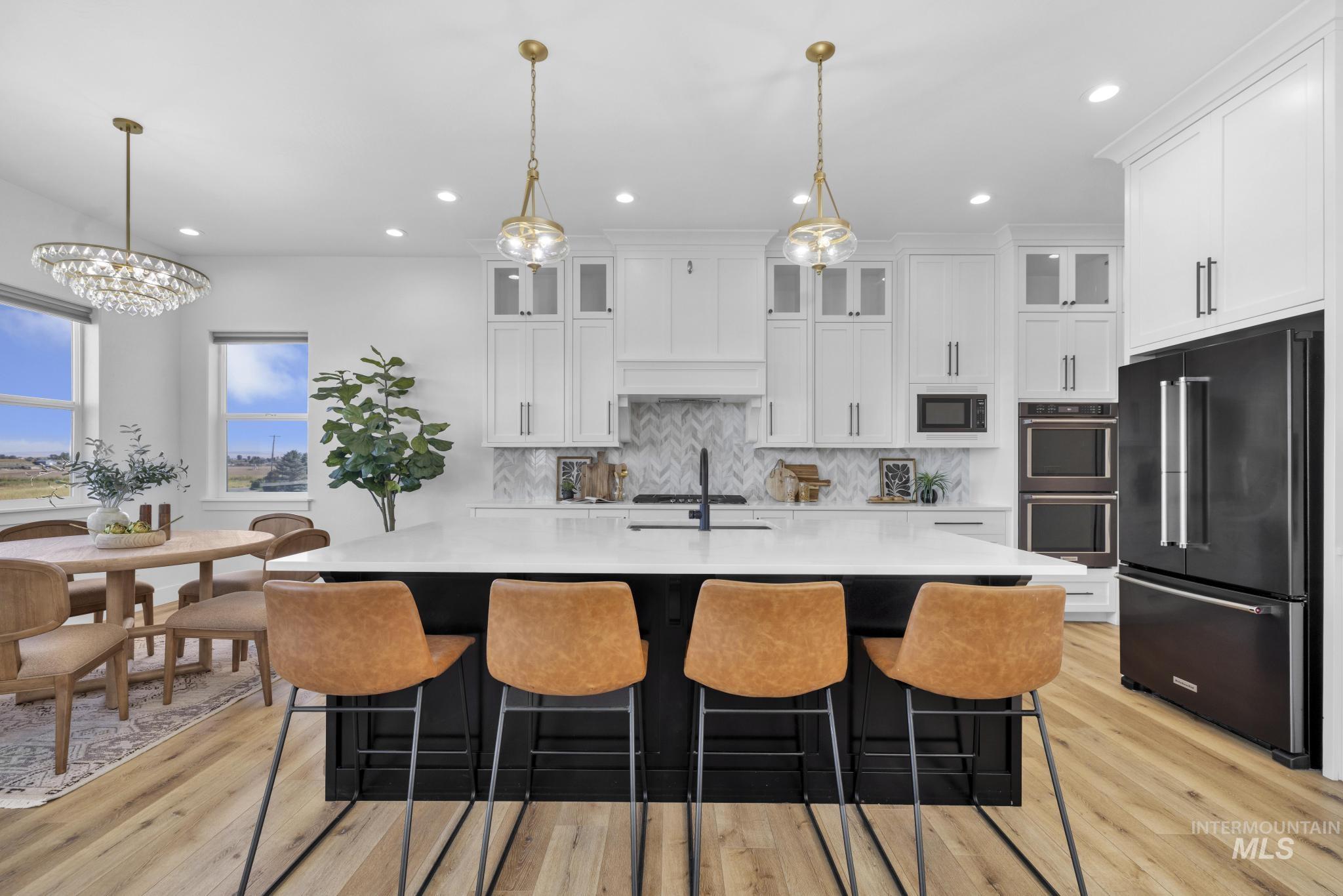 4280 Rim Vista Road Filer, ID 83328 - Photo 10 of 50 Open-concept kitchen featuring an island with a light-toned countertop, white cabinetry with dark hardware, a herringbone tile backsplash, and light wood-finish flooring