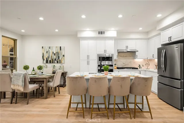 a kitchen with stainless steel appliances kitchen island granite countertop a dining table chairs refrigerator and sink