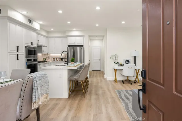 a living room with stainless steel appliances a dining table wooden floor and a view of kitchen
