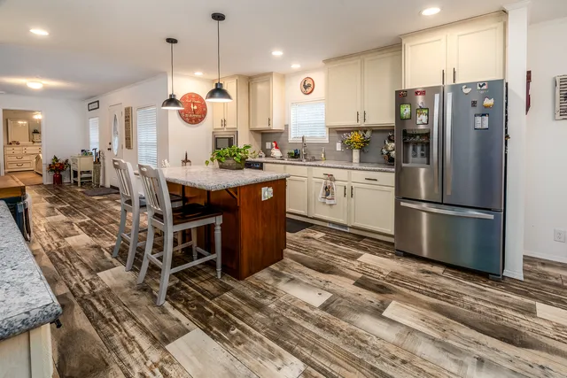 a kitchen with stainless steel appliances granite countertop a refrigerator a sink dishwasher a oven and a dining table with wooden floor