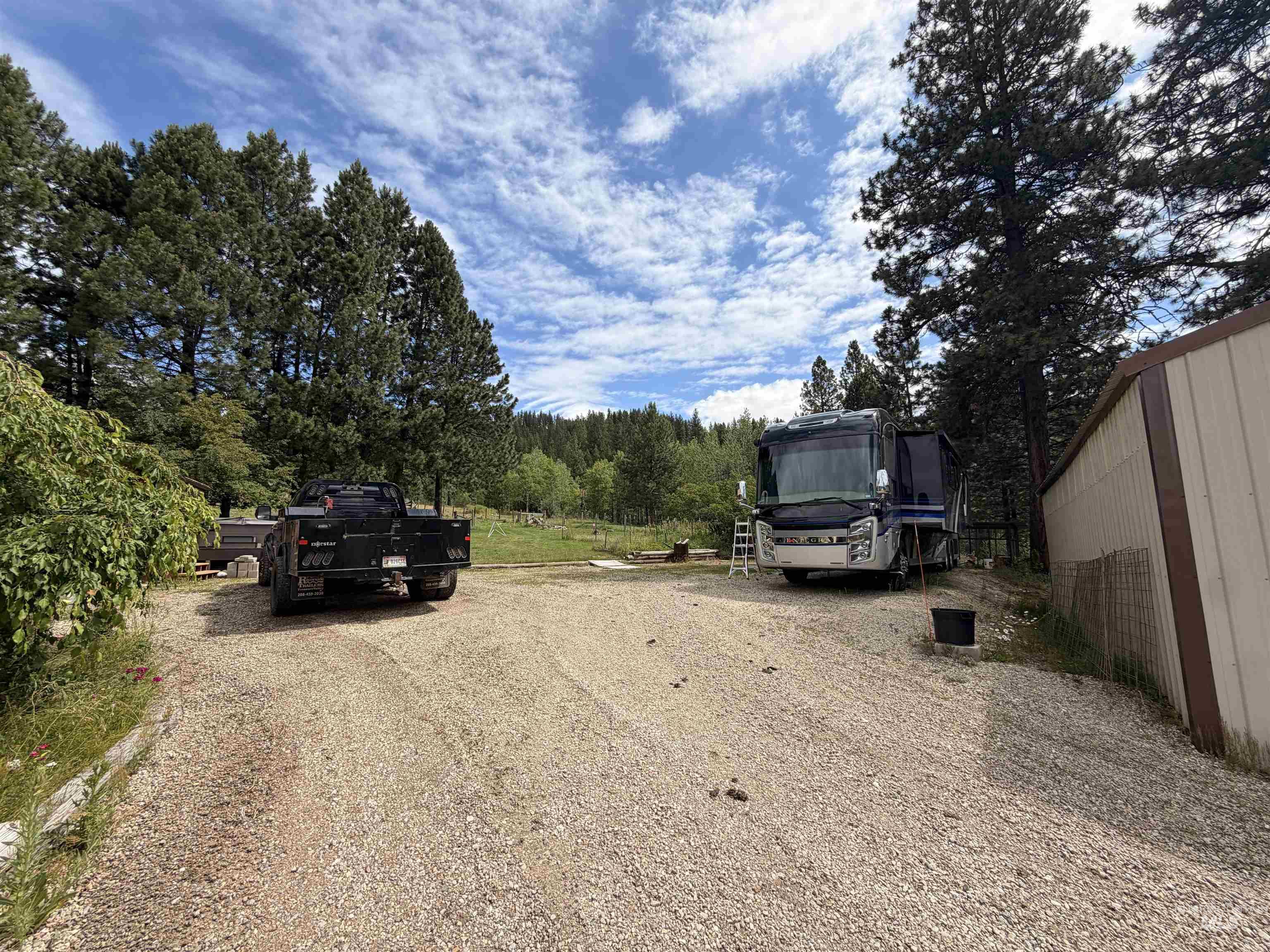 40 Atkin Lane Cascade, ID 83611 - Photo 46 of 46 Gravel driveway providing ample outdoor parking, bordered by mature trees and a metal-sided utility building