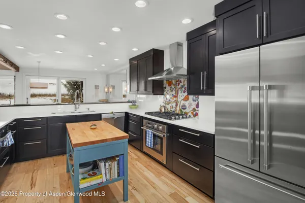 a kitchen with stainless steel appliances granite countertop a refrigerator a sink dishwasher a stove and white countertops with wooden floor
