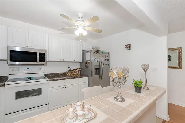 a kitchen with stainless steel appliances kitchen island granite countertop a sink a stove a microwave oven a refrigerator with white cabinets and wooden floor