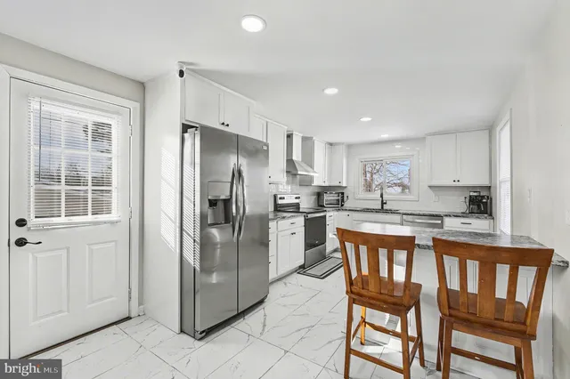 a kitchen with stainless steel appliances granite countertop a refrigerator a stove a sink and white cabinets with wooden floors