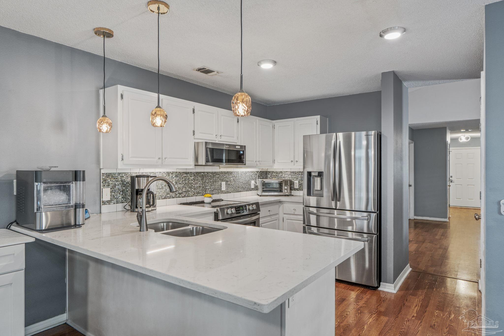 1739 Ivalea Circle Navarre, FL 32566 - Photo 16 of 46 a kitchen with stainless steel appliances a stove a sink a refrigerator a center island a stove and white cabinets with wooden floor