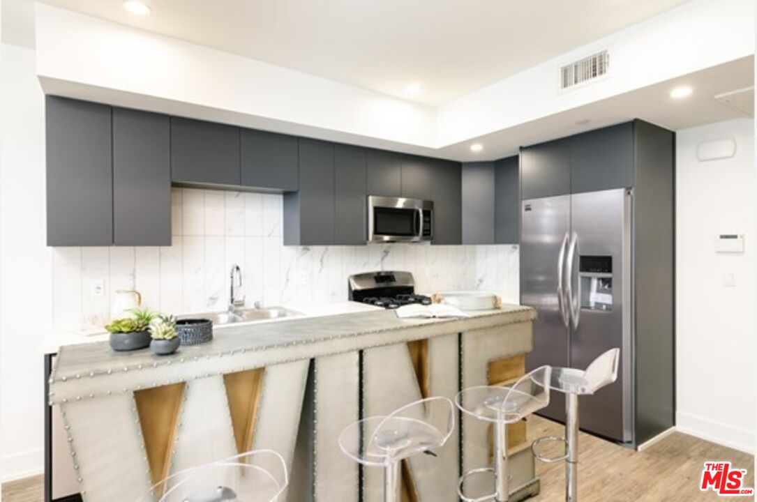 a kitchen with stainless steel appliances a sink a stove a refrigerator cabinets and chairs