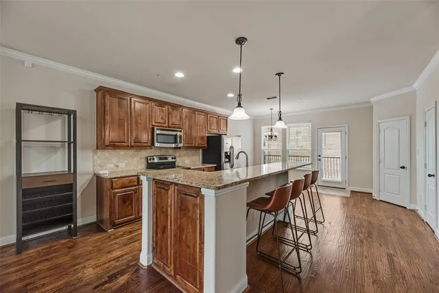 a kitchen with stainless steel appliances granite countertop a stove top oven a refrigerator a sink and a dining table with wooden floor