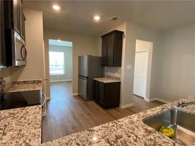 an empty room with wooden floor a kitchen view and a chandelier fan