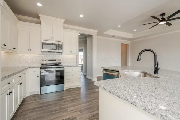 a kitchen with stainless steel appliances kitchen island granite countertop a stove top oven a sink a refrigerator with wooden cabinets and floor