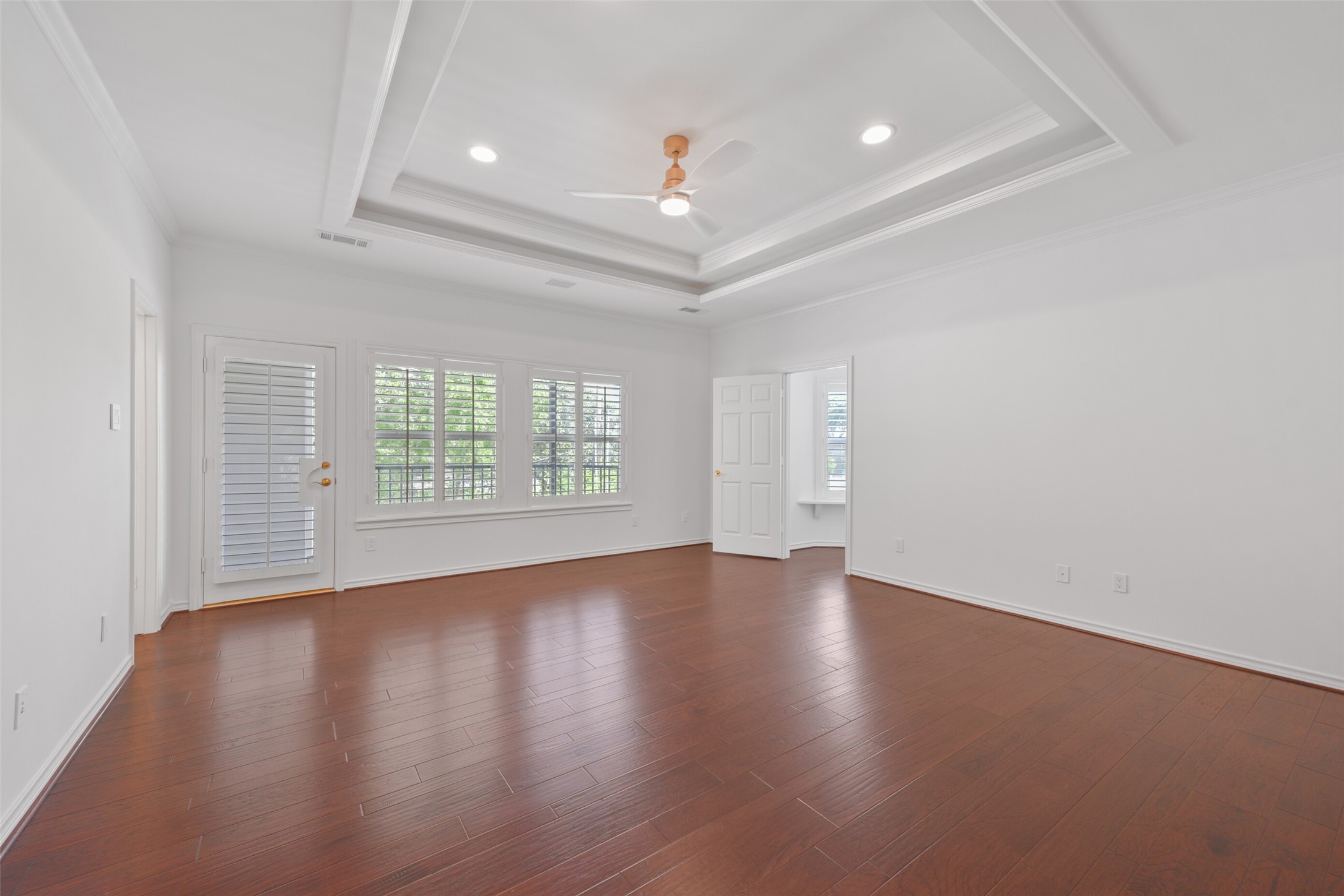 3724 Wroxton Road Houston, TX 77005 - Photo 27 of 40 The primary bedroom with elevated tray ceiling, ceiling fan, hardwoods, and private balcony overlooking the pool.