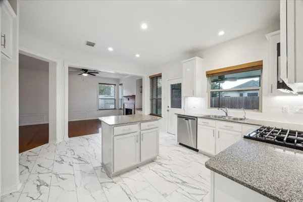 a large white kitchen with granite countertop a sink and dishwasher a stove top oven with wooden floor