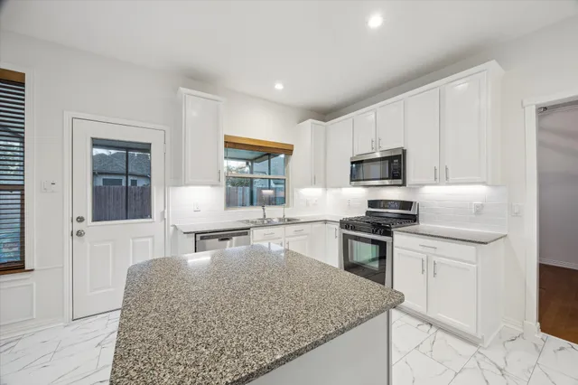 a kitchen with stainless steel appliances granite countertop a stove top oven a sink a dining table and chairs