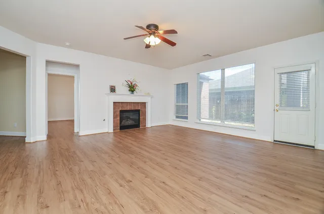 an empty room with wooden floor ceiling fan and windows