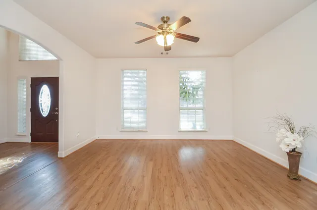 an empty room with wooden floor chandelier fan and windows