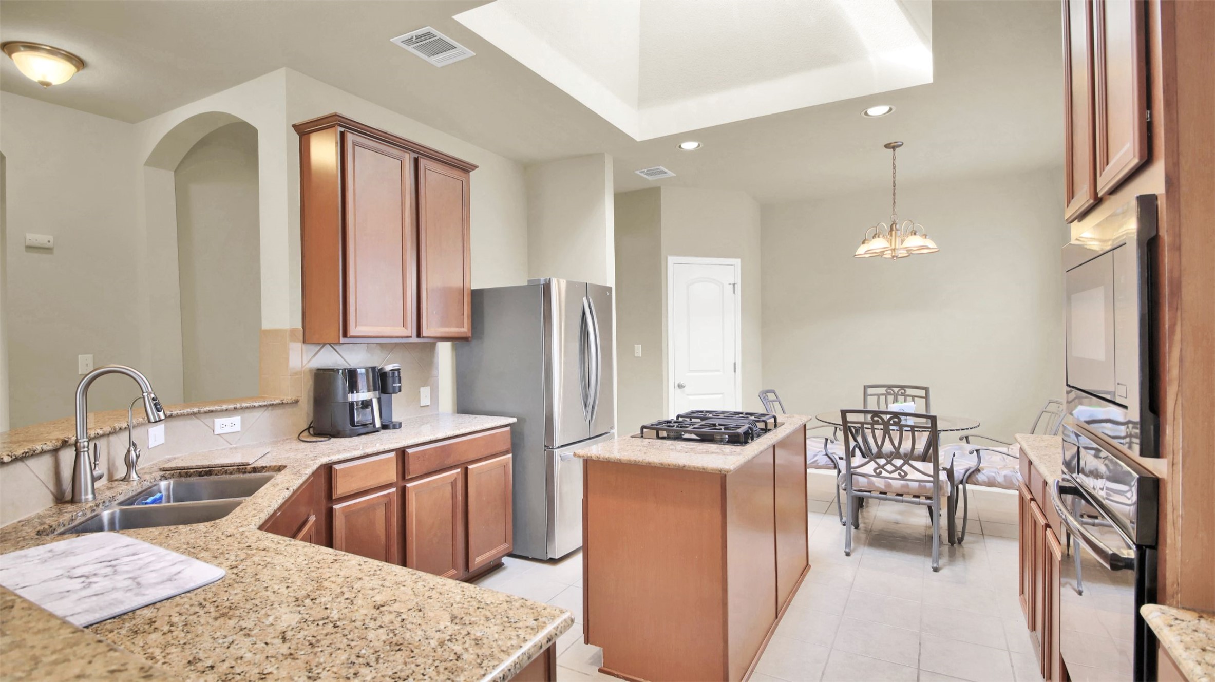 2979 Freemont Street Round Rock, TX 78681 - Photo 16 of 40 Kitchen with a kitchen island, wood finish cabinets, stainless steel appliances, light stone counters, and a raised ceiling